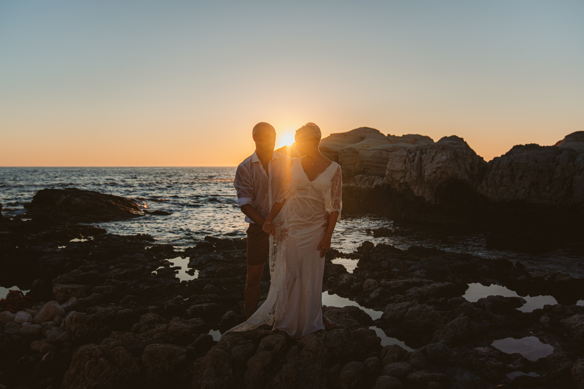 Bride and groom pose beside the Cyprus sea caves at sunset with their trash the dress photographer
